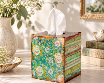 May include: A square tissue box cover featuring a vibrant teal background with a white and pink floral pattern on the front panel, while the side panel displays horizontal stripes in shades of green, pink, and white with a distressed gold finish.