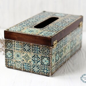 May include: A wooden tissue box cover with a decorative design of blue, green, and gold tiles. The box has a brown wooden lid and a cutout for tissues.