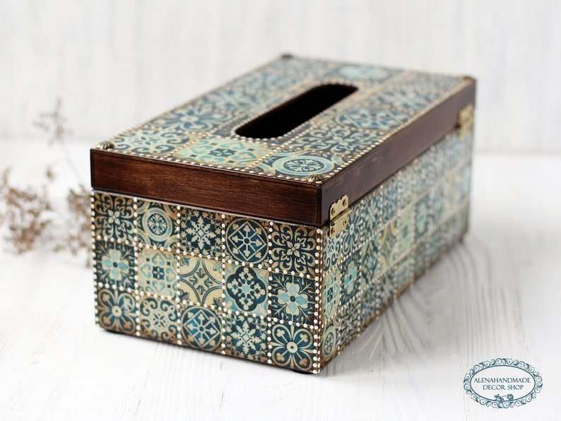 May include: A wooden tissue box cover with a decorative design of blue, green, and gold tiles. The box has a brown wooden lid and a cutout for tissues.