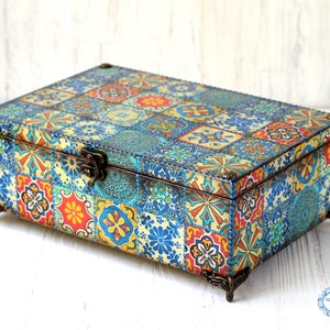 May include: A decorative wooden box with a colourful tile pattern on the lid and sides. The box has a brass latch and sits on four decorative feet.