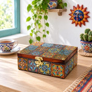 May include: A rectangular wooden box featuring a hinged lid with a gold-tone metal latch. The exterior surfaces are decorated with a vibrant, multi-colored pattern of intricate floral and geometric tiles in shades of blue, yellow, red, and green.