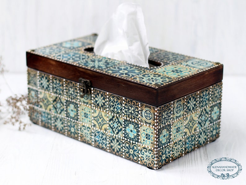 May include: A wooden tissue box cover with a decorative design of blue, green, and gold tiles. The box has a hinged lid with a metal clasp.