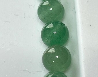 Op de afbeelding: Vijf doorschijnende, ronde, groene kralen zijn verticaal gerangschikt in een witte container. Elke kraal heeft een glad, gepolijst oppervlak met een kleine kleurvariatie. De kralen lijken van een natuursteen te zijn gemaakt.
