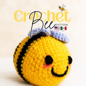 Puede incluir: Un juguete de abeja tejido a ganchillo redondo con rayas amarillas y negras, alas azul claro, ojos negros y una sonrisa bordada con mejillas rosadas. El texto dice Crochet Bee PATTERN con banderas de EE. UU. y México y @Seluanna_studio.