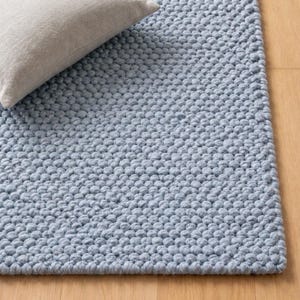 Könnte beinhalten: Ein hellblaues, strukturiertes Rug mit einem noppenartigen, geschlungenen Design. Ein neutralfarbenes Kissen liegt auf dem Rug, der auf einem hellen Holzboden liegt. Die Textur des Rugs ist deutlich sichtbar.