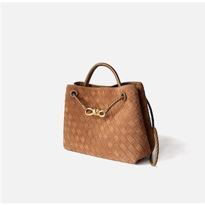 May include: A brown woven leather handbag with a top handle and a detachable shoulder strap. The bag features a gold-toned clasp and braided leather details. The bag is approximately 10 inches wide and 8 inches tall.