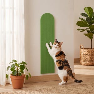 Puede incluir: Un rascador para gatos vertical y montado en la pared de color verde, con una parte superior redondeada y una superficie texturizada con ranuras. El panel rectangular está fijado a una pared plana, ofreciendo un área para rascar.