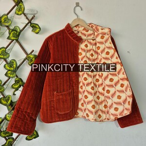 May include: A rust-colored quilted jacket with a corduroy texture. The jacket features a contrasting floral pattern lining in cream and orange. The text "PINKCITY TEXTILE" is printed on the jacket.