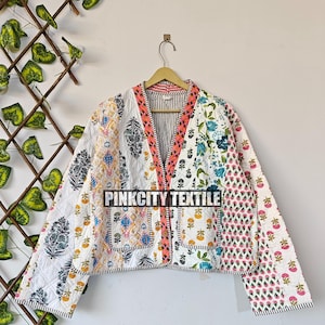 May include: A patchwork jacket with a variety of floral and geometric patterns in white, blue, pink, and orange. The jacket has a V-neck, two pockets, and is hanging on a wooden hanger. The text "PINKCITY TEXTILE" is visible.