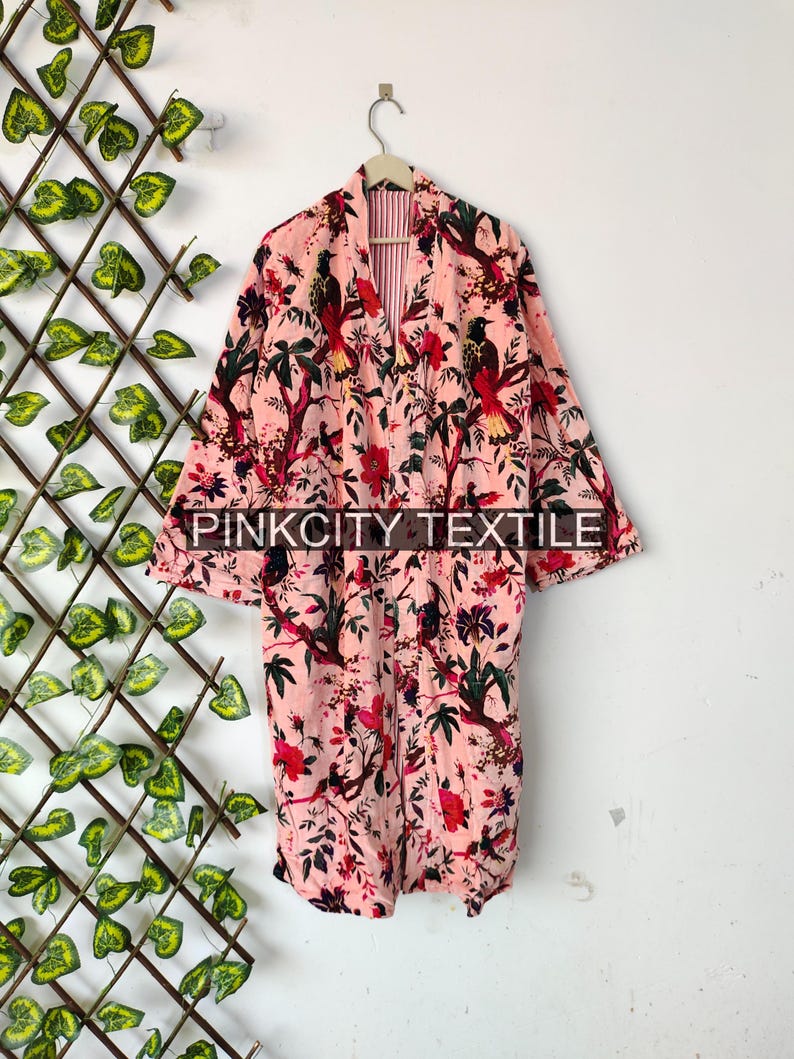 May include: A pink floral print robe with a bird and floral design. The robe has long sleeves and a belt. The text "PINKCITY TEXTILE" is printed on the bottom of the robe.