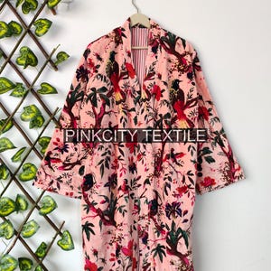 May include: A pink floral print robe with a bird and floral pattern. The robe has long sleeves and is hanging on a wooden hanger. The text "PINKCITY TEXTILE" is visible on the robe.