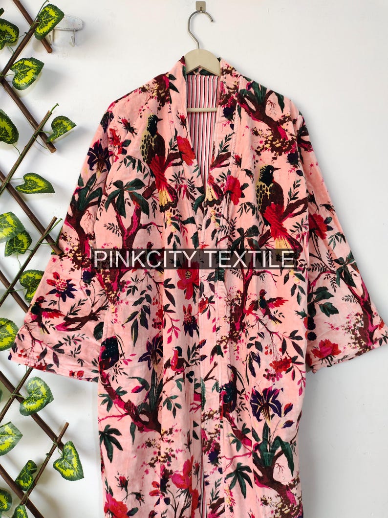 May include: A pink floral robe with a bird and tree design. The robe has long sleeves and a striped interior. The text "PINKCITY TEXTILE" is printed on the robe.