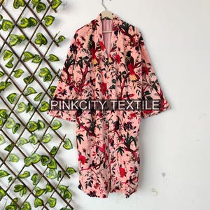 May include: A pink floral print robe with a bird and floral pattern. The robe is hanging on a wooden hanger. The text "PINKCITY TEXTILE" is printed on the robe.