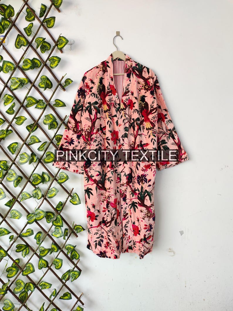 May include: A pink floral print robe with a bird and floral pattern. The robe is hanging on a wooden hanger. The text "PINKCITY TEXTILE" is printed on the robe.
