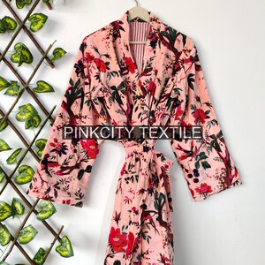 May include: A pink floral print robe with long sleeves and a matching belt. The robe features a vibrant pattern of red flowers, green leaves, and birds against a light pink background. The text "PINKCITY TEXTILE" is visible on the robe.