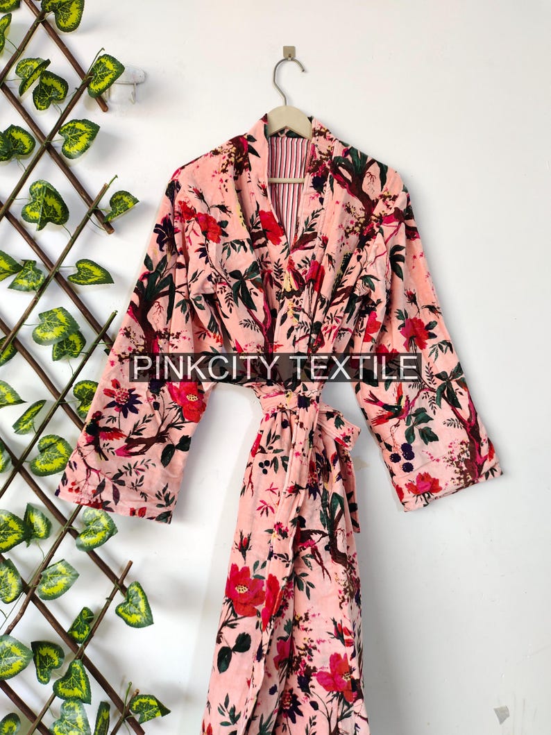 May include: A pink floral print robe with long sleeves and a matching belt. The robe features a vibrant pattern of red flowers, green leaves, and birds against a light pink background. The text "PINKCITY TEXTILE" is visible on the robe.