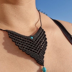 Può includere: Una collana in macramè nero caratterizzata da un design a cordoncino intrecciato a forma di V. Il pezzo è impreziosito da una piccola perlina color turchese incastonata al centro e da due perline rotonde turchesi più grandi pendenti.