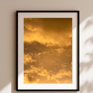Könnte beinhalten: Gerahmter Druck mit einem Himmel voller goldener Wolken. Das Kunstwerk wird in einem schwarzen Rahmen mit weißem Passepartout präsentiert, was die Wirkung des Bildes verstärkt. Die Fotografie fängt die Textur und Tiefe der Wolken ein.