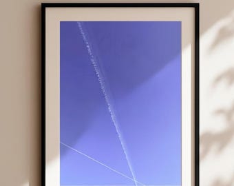 Puede incluir: Impresión artística enmarcada que presenta un cielo azul vibrante con una estela blanca y una fina línea blanca. La obra de arte está encerrada en un marco negro con un passe-partout blanco, creando una estética moderna. La impresión se exhibe en una pared de color neutro.