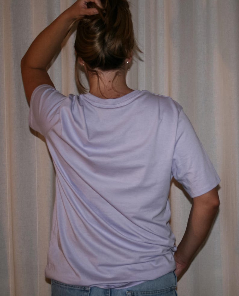 Puede incluir: Una camiseta de manga corta en color lavanda claro con cuello redondo. La prenda se combina con unos vaqueros de mezclilla azul. El tejido es liso y opaco, con un corte est&aacute;ndar, mangas cortas y un dobladillo recto en la parte inferior.