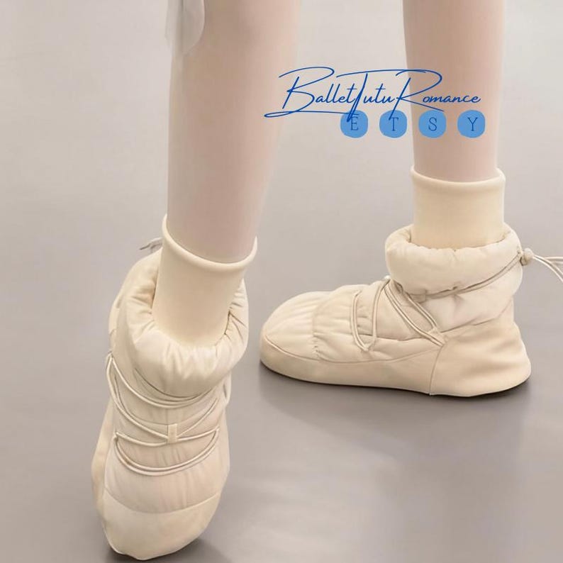 May include: Cream-colored ballet bootie slippers with quilted texture and lace-up detail. The slippers are worn with off-white tights. The text "Ballet Tutu Romance" is in the upper center of the image.