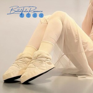May include: Cream-colored ballet warm-up boots with black soles. The boots have a quilted design and are worn with matching leg warmers. The Etsy shop name "Ballet Tutu Romance" is in the upper left corner.