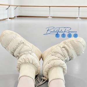 May include: A pair of beige snow boots with a quilted design and drawstring closure. The boots have a ribbed cuff and are set against a light background. The text "Ballet Tutu Romance" is visible in the image.