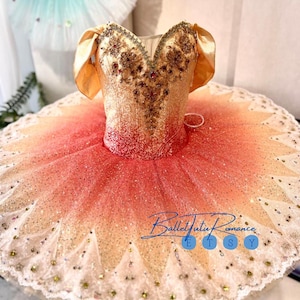 Könnte beinhalten: Ein Balletttutu mit einem goldenen Oberteil und einem mehrschichtigen Rock, der von Pfirsich zu Weiß verblasst. Das Oberteil ist mit goldenen und roten Akzenten verziert. Der Rock ist mit Glitzer bedeckt und hat eine Spitzenborte. Der Etsy-Shop-Name "BalletTutu Romance" ist sichtbar.