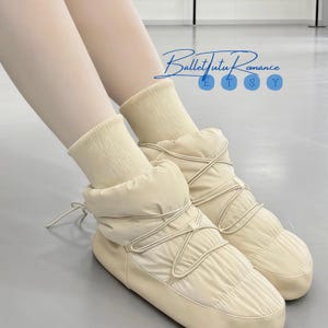 May include: Cream-colored quilted snow boots with a lace-up design. The boots have a puffy, padded appearance and are paired with cream-colored socks. The image includes the text "Ballet Tutu Romance" in a script font.