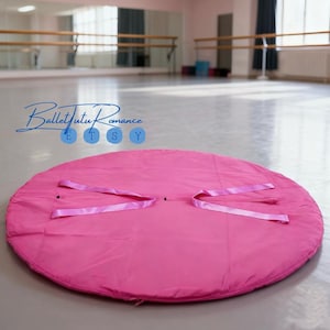 Może przedstawiać: Jasnoróżowa, okrągła mata do zabawy z dołączonymi różowymi wstążkami. Mata leży na jasnej podłodze w studio tańca. Tekst "Ballet Tutu Romance" jest widoczny w tle.
