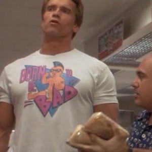 Könnte beinhalten: Ein weißes T-Shirt mit einem Aufdruck, der "Born to be Bad" in Pink und Blau zeigt. Die Grafik zeigt eine Cartoonfigur mit Sonnenbrille. Das T-Shirt wird von einer Person getragen.