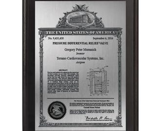 Puede incluir: Placa de patente enmarcada de los Estados Unidos para una válvula de alivio diferencial de presión. La placa presenta el texto "THE UNITED STATES OF AMERICA" y el número de patente 9.435.450. También se muestra el nombre del inventor, Gregory Peter Muennich.