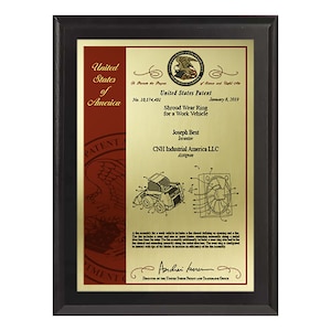 May include: A framed United States patent plaque. The plaque features a gold-colored plate with text and diagrams, including the title "Shroud Wear Ring for a Work Vehicle." The frame is black, and the plaque includes the United States Patent seal.
