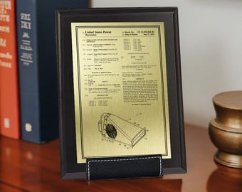 Puede incluir: Una placa de patente de Estados Unidos enmarcada con una placa de metal dorada. La placa presenta un marco negro y un soporte de polipiel negro. Los detalles de la patente están impresos en tinta negra.