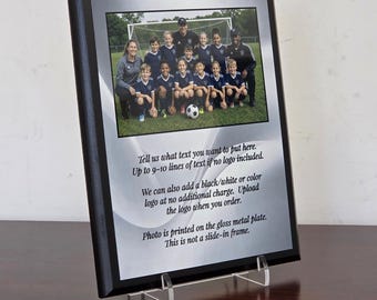 May include: A rectangular black wooden plaque featuring a glossy silver metal plate. The top section displays a color photograph of a youth soccer team on a field. The lower section contains printed text regarding customization and printing details.