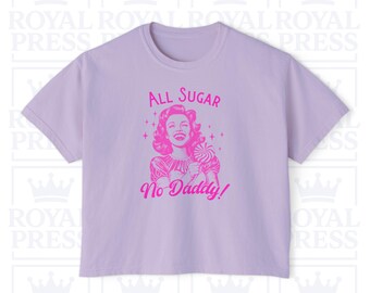 May include: A light purple t-shirt with a pink graphic. The graphic features a vintage illustration of a woman holding a lollipop, with the text "All Sugar No Daddy!" above and below the image.
