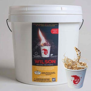May include: A large white plastic bucket with a black handle and a label reading Wilson Natural Fire Starter, featuring a graphic of a burning cup. Beside it sits a smaller white paper cup filled with wood shavings and a red flame logo.