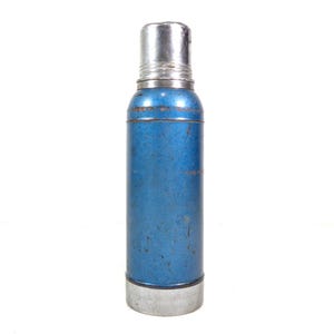 Pode incluir: Uma garrafa t&eacute;rmica azul e prateada vintage. O corpo cil&iacute;ndrico &eacute; azul desbotado com a parte superior e inferior prateadas. A garrafa t&eacute;rmica tem uma tampa de rosca e parece ser feita de metal. O design geral sugere um estilo cl&aacute;ssico e retro.