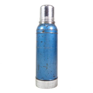 Pode incluir: Termo de metal azul vintage com tampa e base prateadas. A garrafa cil&iacute;ndrica mostra sinais de desgaste, com arranh&otilde;es vis&iacute;veis e uma cor ligeiramente desbotada. O termo foi projetado para manter l&iacute;quidos quentes ou frios.