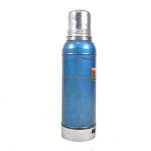 Pode incluir: Uma garrafa t&eacute;rmica Stanley azul vintage com tampa e base prateadas. A garrafa t&eacute;rmica tem formato cil&iacute;ndrico e um pequeno r&oacute;tulo com texto. O exterior mostra sinais de desgaste, indicando sua idade.