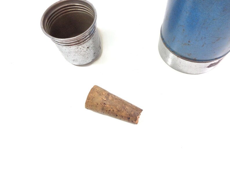 Pode incluir: Vista a&eacute;rea de uma garrafa t&eacute;rmica azul e prateada com tampa prateada e rolha de corti&ccedil;a. A garrafa t&eacute;rmica &eacute; azul com uma faixa prateada. A tampa &eacute; prateada e canelada. A rolha de corti&ccedil;a &eacute; castanha.