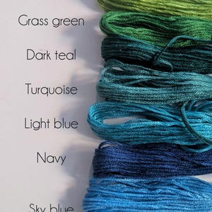 May include: A collection of embroidery floss skeins arranged in a vertical column, featuring shades of mint green, apple green, grass green, dark teal, turquoise, light blue, navy, sky blue, and cornflower, with each colour labelled by its name.