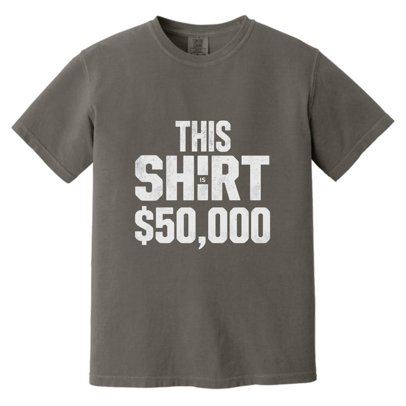 Puede incluir: Una camiseta gris con el texto "THIS SHIRT IS $50,000" en letras blancas desgastadas. La camiseta es de cuello redondo y parece estar hecha de un material suave y c&oacute;modo. La est&eacute;tica general es informal y humor&iacute;stica.