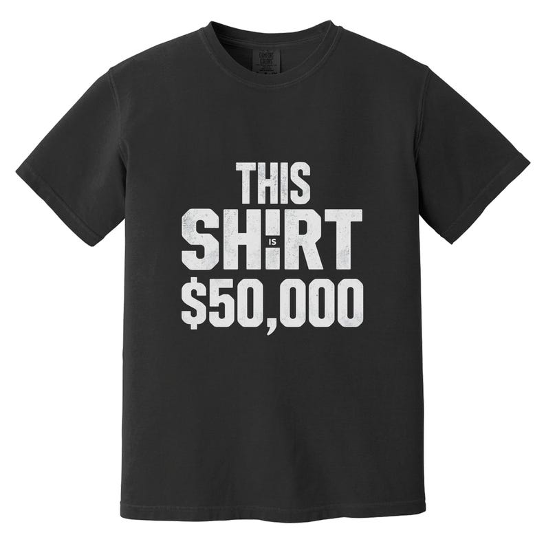 Puede incluir: Camiseta negra con el texto blanco "THIS SHIRT IS $50,000". El texto est&aacute; en letras blancas de estilo desgastado. La camiseta tiene cuello redondo y mangas cortas. La tela parece ser una mezcla de algod&oacute;n suave.
