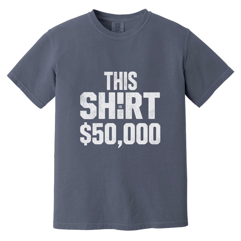 Puede incluir: Una camiseta azul pizarra con el texto "THIS SHIRT IS $50,000" impreso en blanco, con letras desgastadas. La camiseta tiene cuello redondo y mangas cortas. La tela parece ser una suave mezcla de algod&oacute;n.
