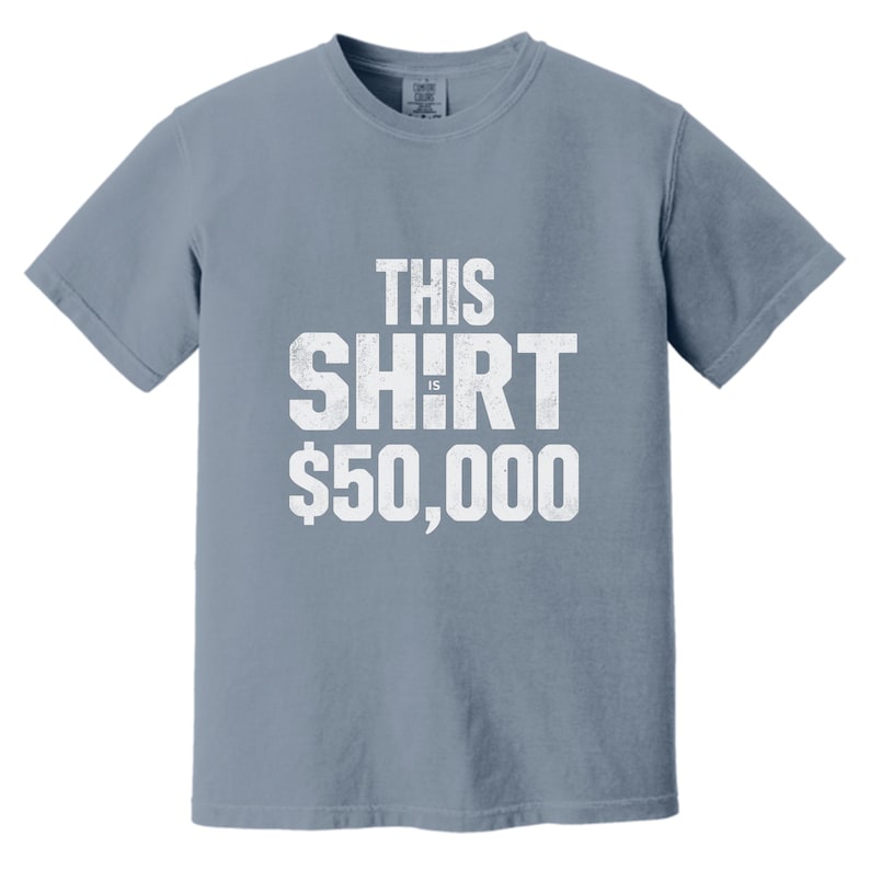 Puede incluir: Camiseta azul polvoriento con el texto blanco "THIS SHIRT IS $50,000". La camiseta tiene mangas cortas y cuello redondo. El texto tiene un aspecto vintage.