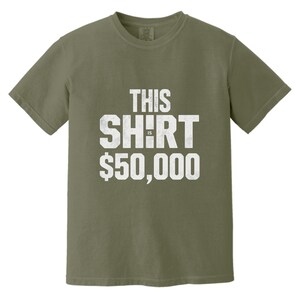 Puede incluir: Camiseta verde oliva con el texto "THIS SHIRT IS $50,000" en letras blancas desgastadas. La camiseta es de cuello redondo y manga corta.