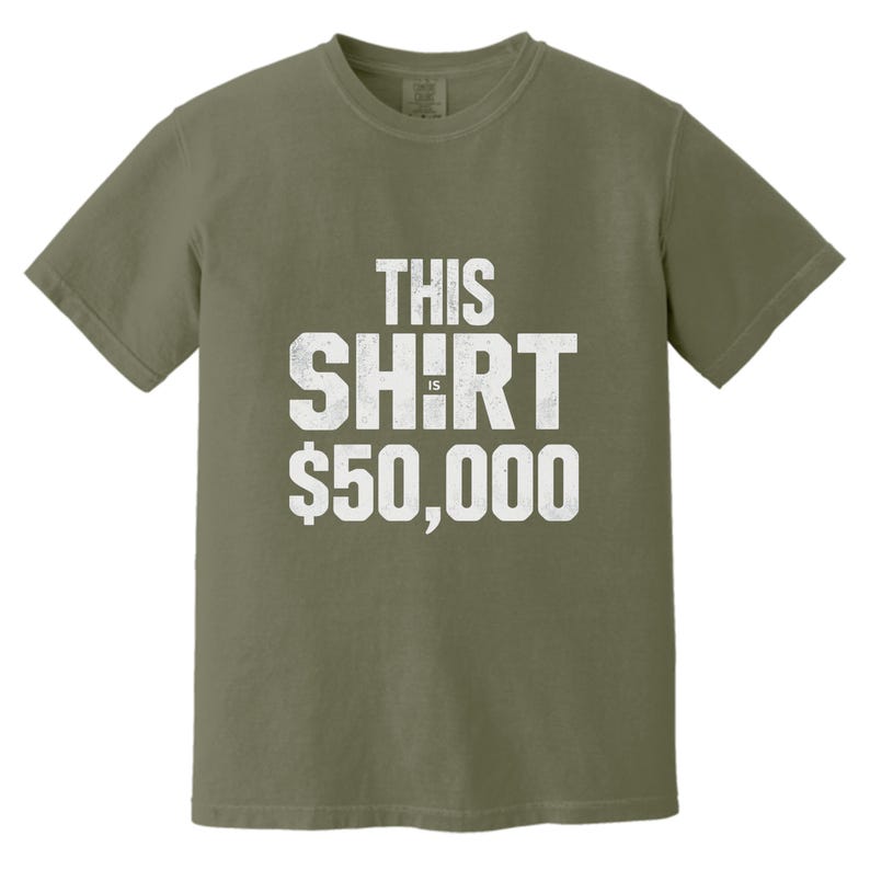 Puede incluir: Camiseta verde oliva con el texto "THIS SHIRT IS $50,000" en letras blancas desgastadas. La camiseta es de cuello redondo y manga corta.