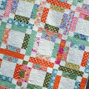 May include: A colorful patchwork quilt with a white background. The quilt is made up of squares of different fabrics, each with a different pattern. The fabrics are mostly floral and geometric patterns in shades of orange, green, blue, and pink.