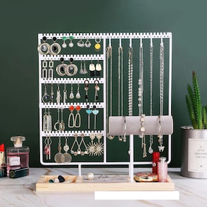 May include: White metal jewelry organizer with multiple earring and necklace display options. Features a wooden base with small compartments for rings and other accessories. Includes a small succulent plant in a decorative pot.